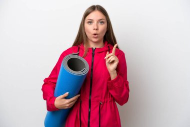 Genç bir kadın yoga derslerine giderken beyaz arka planda bir minder tutuyor.   