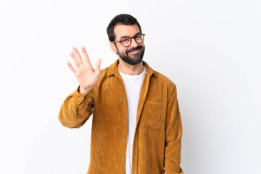 Beyaz tenli, sakallı, kadife ceket giyen yakışıklı bir adam izole edilmiş beyaz arka planda mutlu bir ifadeyle selam veriyor.