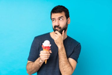 Kornet dondurması ile izole edilmiş mavi arka planı olan genç bir adamın şüpheleri ve kafa karıştırıcı bir yüz ifadesi var.
