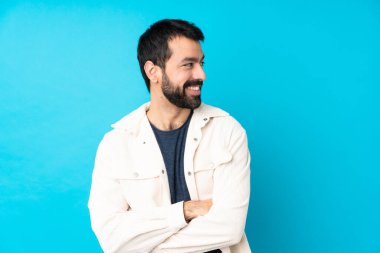 Beyaz kadife ceketli yakışıklı genç adam izole edilmiş mavi arka planda kolları bağlı ve mutlu.