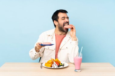 Masada kahvaltılık waffle ve milkshake yiyen bir adam.