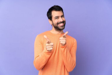 İzole edilmiş mor arka planda beyaz, yakışıklı bir adam öne doğru bakıyor ve gülümsüyor.