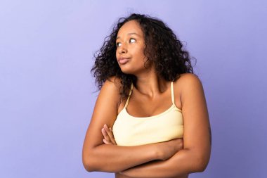 Kübalı genç bir kız mor arka planda izole edilmiş. Omuzlarını kaldırırken şüpheli hareketler yapıyor.