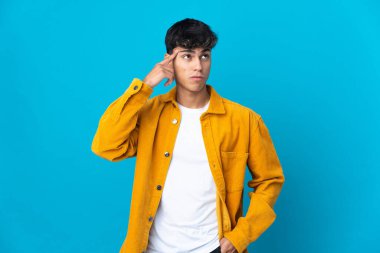 Soyutlanmış mavi arka planda genç bir adam deliliğin jestini yapıyor. Parmağını kafaya koyuyor.