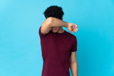 Genç Venezuelalı adam mavi arka planda izole edilmiş gözleri elleriyle kaplayan