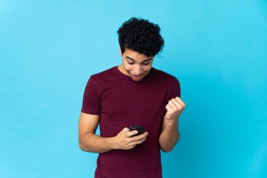 Genç Venezuelalı adam mavi arka planda izole edildi. Şaşırdı ve bir mesaj gönderiyor.