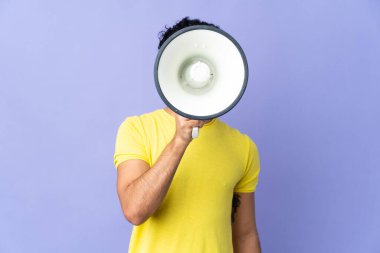 Genç Venezuelalı bir adam mor arka planda izole edilmiş bir şekilde megafondan bir şey duyurmak için bağırıyor.