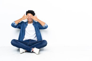 Venezuelalı bir adam yerde oturuyor, elleriyle gözlerini kapatıyor.