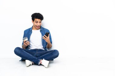 Venezuelalı bir adam kahve alıp götürmek için yerde oturuyor. Bir de cep telefonu.