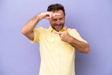 Orta yaşlı beyaz bir adam, mor arka planda izole edilmiş, odaklanmış bir yüz. Çerçeve sembolü