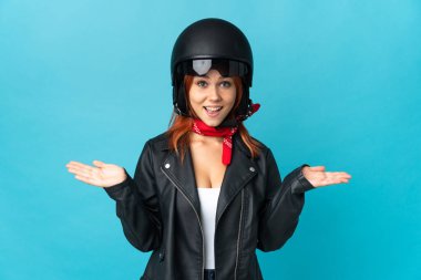 Genç motorcu kız mavi arka planda izole edilmiş ve şok olmuş bir yüz ifadesi var.