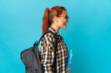 Genç Rus kız öğrenci mavi arka planda izole edilmiş. Yan pozisyonda gülüyor.