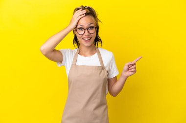 Restoran garsonu. Rus kız sarı arka planda izole edilmiş. Şaşırmış ve işaret ediyor.