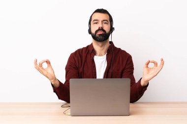 Tele pazarlamacı beyaz adam kulaklıkla çalışıyor ve dizüstü bilgisayarı zen pozunda..
