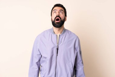 Sakallı, ceketli, soyutlanmış bir beyaz adam yukarı bakıyor ve şaşırmış bir ifadeyle bakıyor.