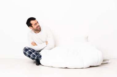 Beyaz, pijamalı bir adam kolları bağlı ve mutlu bir şekilde yerde oturuyor.