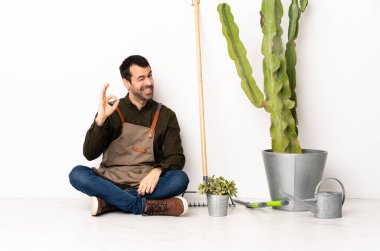 Bahçıvan içeride yerde oturuyor. Parmaklarıyla 