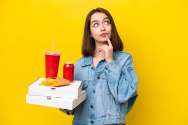 Ukraynalı genç bir kadın elinde fast food tutarken sarı arka planda izole edilmiş bir şekilde yukarı bakarken şüpheleri var.