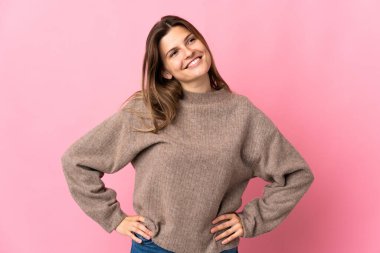 Genç Slovak kadın pembe arka planda soyutlanmış kollarıyla kalçasında poz veriyor ve gülümsüyor