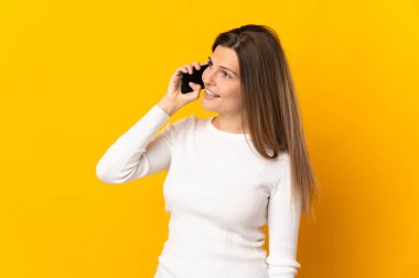 Genç Slovak kadın sarı arka planda izole edilmiş cep telefonuyla sohbet ediyor.