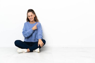 Yerde oturan genç bir kadın bir ürün sunmak için yan tarafı işaret ediyor.