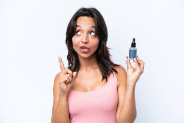 Beyaz arka planda serumu tutan genç İspanyol kadın bir fikrin parmağı yukarı kaldırdığını düşünüyor.
