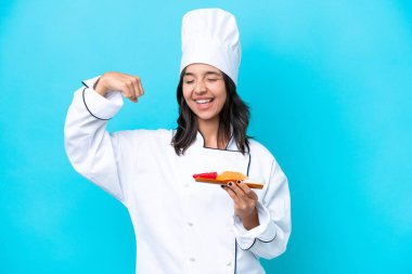 Mavi arka planda saşimi tutan genç İspanyol şef kadın güçlü bir jest yapıyor.