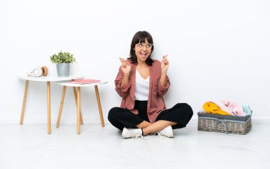 Genç melez kadın, katlanan giysiler, beyaz arka planda izole bir şekilde oturuyor.