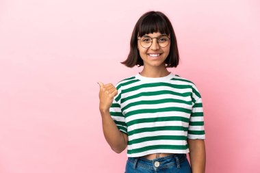 Pembe arka planda izole edilmiş genç melez kadın bir ürünü sunmak için kenarı işaret ediyor.