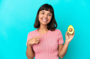 Mavi arka planda avakado tutan melez bir kadın bir ürünü sunmak için yan tarafı işaret ediyor.