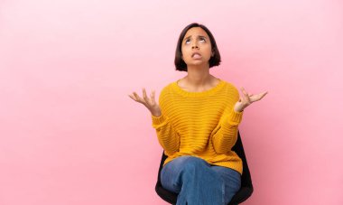 Pembe arka planda izole edilmiş bir sandalyede oturan genç melez kadın bunalımda.