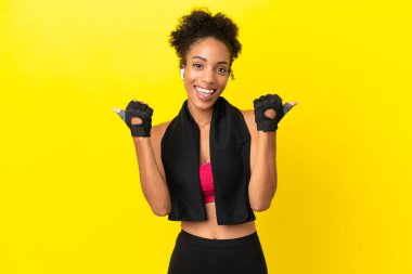 Genç Afrikalı sporcu kadın sarı arka planda izole edilmiş. Baş parmakları havada ve gülümsüyor.