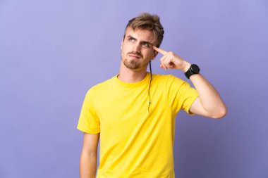 Mor arka planda soyutlanmış genç, yakışıklı sarışın adam deliliğin jestini yapıyor. Parmağını kafaya koyuyor.