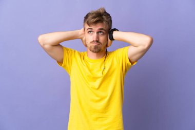 Mor arka planda izole edilmiş yakışıklı sarışın adam hayal kırıklığına uğramış ve kulaklarını kapatmış.