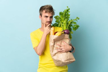 Sarışın bir adam mavi arka planda izole edilmiş bir paket yiyecek alıyor. Yan tarafa bakıyor ve gülümsüyor.