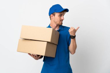 Beyaz arka planda izole edilmiş genç teslimatçı sarışın adam bir ürün sunmak için kenarı işaret ediyor