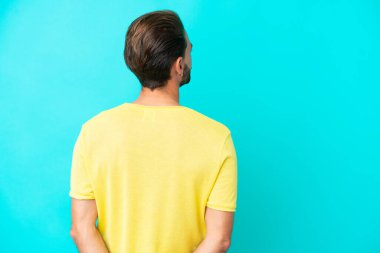 Kafkasyalı genç adam mavi arka planda izole edilmiş ve arkasına bakıyor.