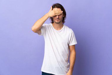 Mor arka planda izole edilmiş genç ve yakışıklı bir adam gözleri elleriyle kapatıyor. Bir şey görmek istemiyorum.