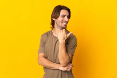 Sarı arka planda izole edilmiş genç yakışıklı bir adam bir ürün sunmak için kenarı işaret ediyor.