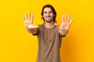 Sarı arka planda izole edilmiş genç yakışıklı adam parmaklarıyla ona kadar sayıyor.