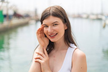 Genç, güzel bir kadın açık havada, mutlu bir ifadeyle.