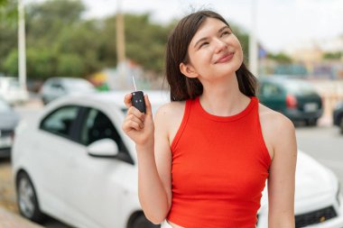 Genç, güzel Ukraynalı bir kadın arabanın anahtarlarını elinde tutuyor ve gülümserken yukarı bakıyor.