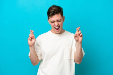 Genç yakışıklı Brezilyalı adam mavi arka planda izole edilmiş ve parmakları çapraz