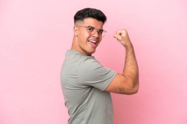 Pembe arka planda izole edilmiş beyaz, yakışıklı genç bir adam güçlü bir jest yapıyor.
