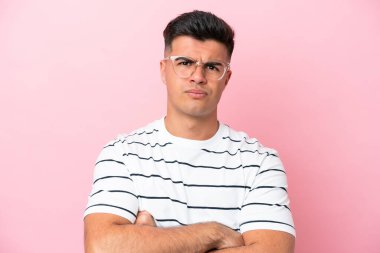 Pembe arka planda gözlüklü ve kolları çaprazlanmış beyaz, yakışıklı genç bir adam.