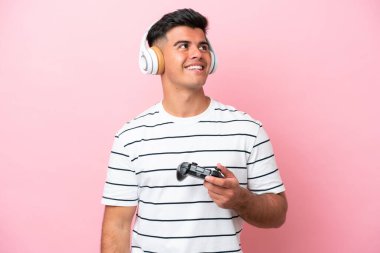 Pembe arka planda izole edilmiş bir bilgisayar oyunu kontrolörüyle oynayan genç yakışıklı bir adam yukarı bakarken bir fikir düşünüyor.