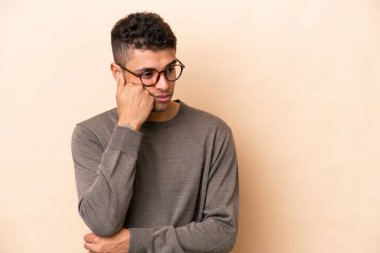 Genç Brezilyalı adam bej arka planda izole edilmiş, yorgun ve sıkılmış bir ifadeyle.