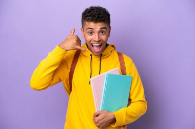 Mor arka planda izole edilmiş Brezilyalı genç bir öğrenci telefon jesti yapıyor. Bana geri dönüş işareti ver.