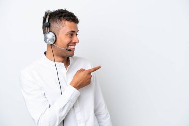 Tele pazarlamacı Brezilyalı adam beyaz arka planda izole edilmiş bir kulaklıkla çalışıyor. Parmakla işaret ediyor ve bir ürün sunuyor.