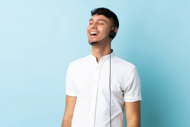 Kolombiyalı tele-pazarlamacı, kulaklıkla çalışıyor, gülerek.